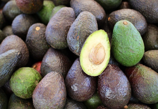 Pile of whole avocados with one half on top