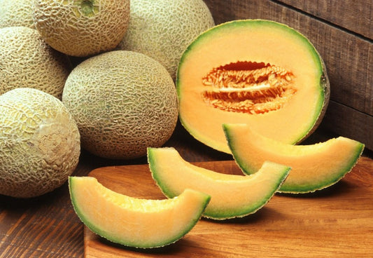 Whole, halved, and sliced cantaloupe on a cutting board