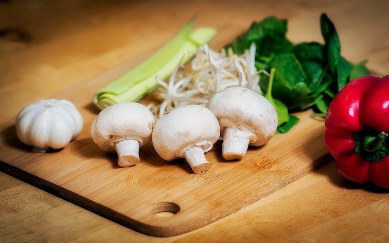 Four white mushrooms on a cutting board with other vegetables